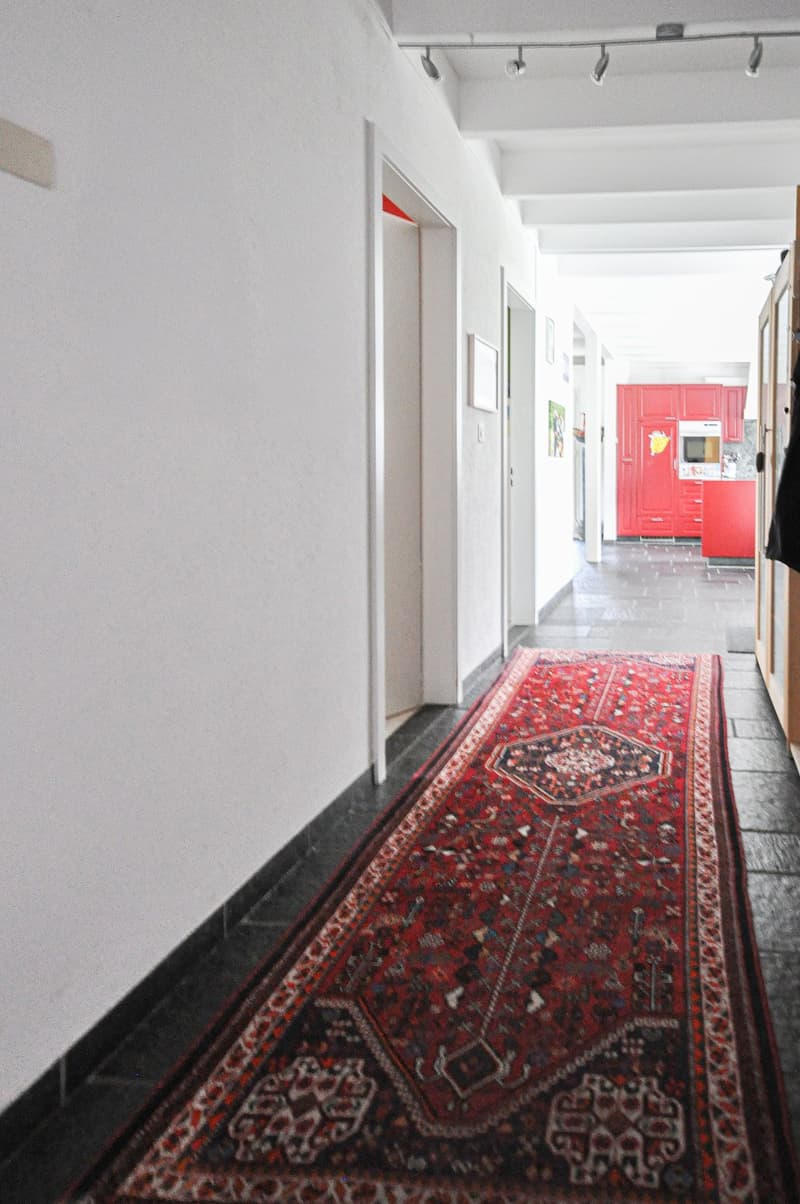 White walls, black tiles, red rug, hallway leading to the kitchen