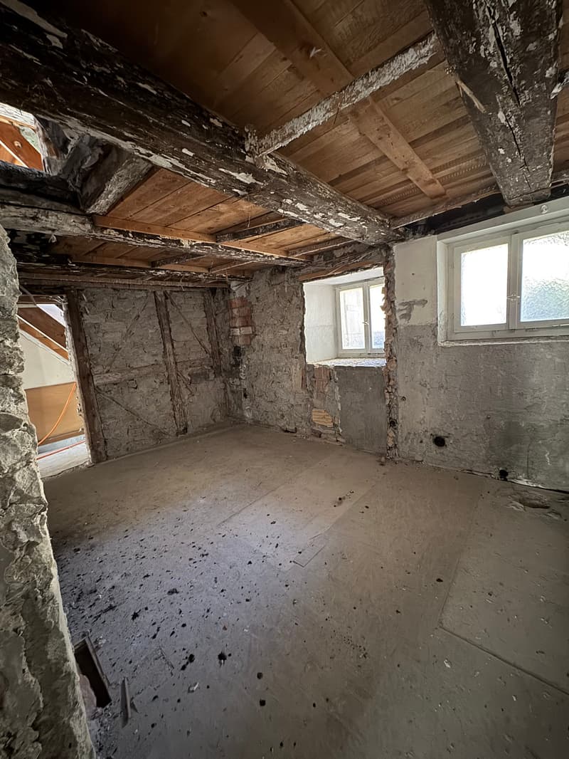empty room with wooden beams, concrete floor, small windows, damaged walls