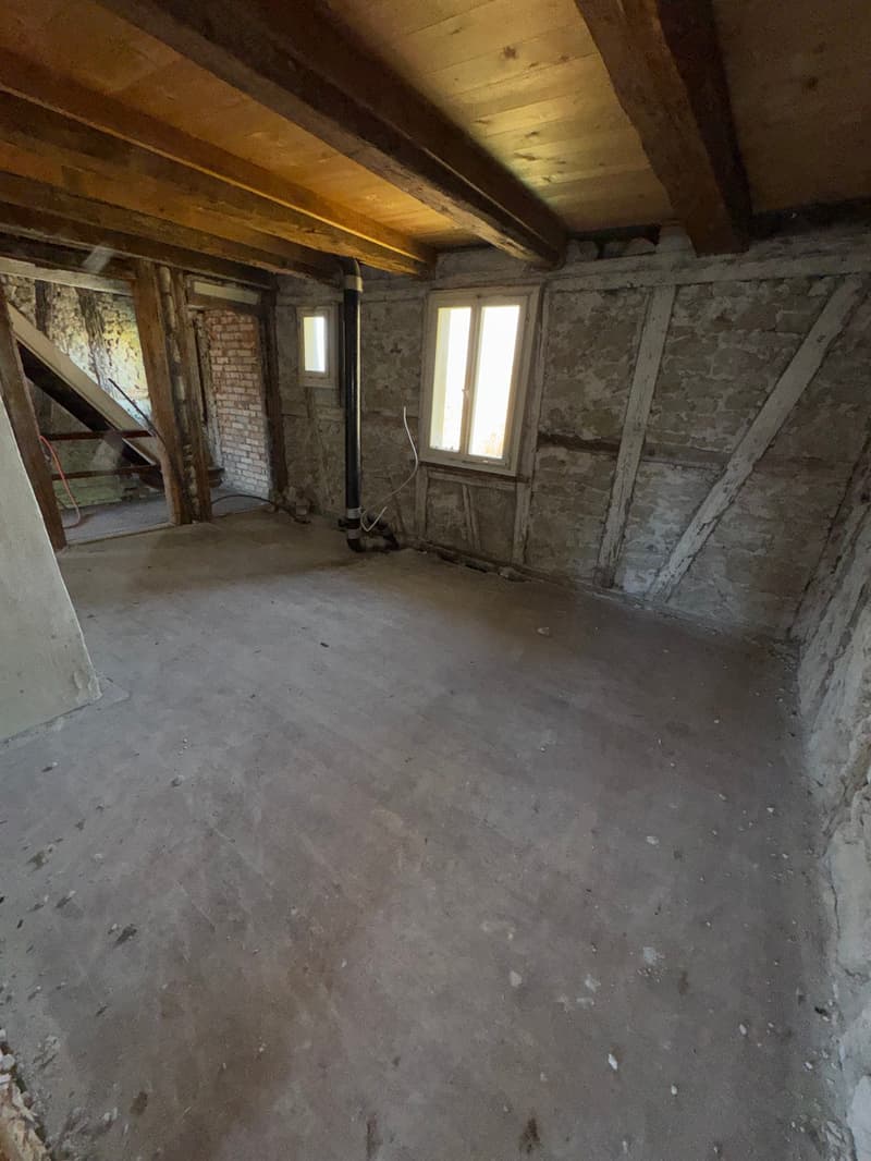 empty room, stone and brick walls, large windows, wooden beams on ceiling
