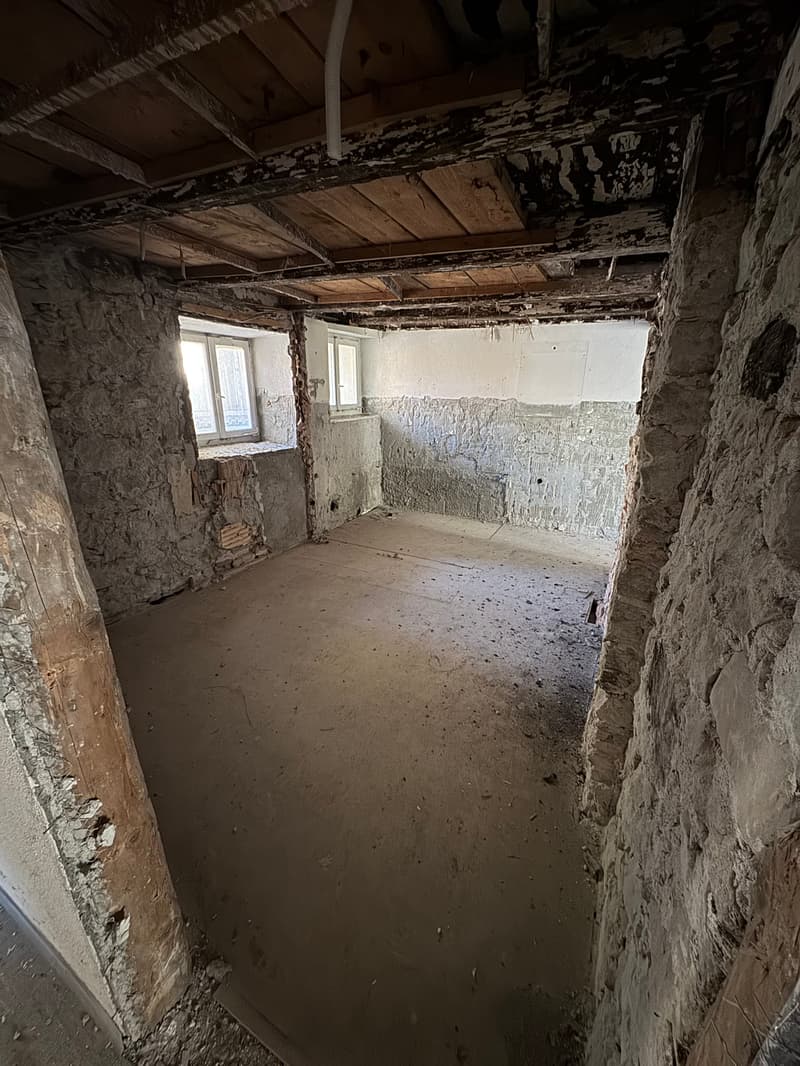 empty room, stone walls, bare concrete floor, two windows, exposed wooden beams, weathered wooden column