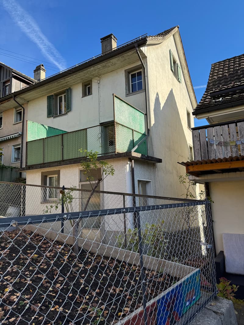 3 story house, white walls, green balconies, chain link fence in the front