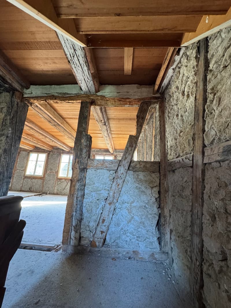exposed wooden beams, stone walls, concrete floor, windows
