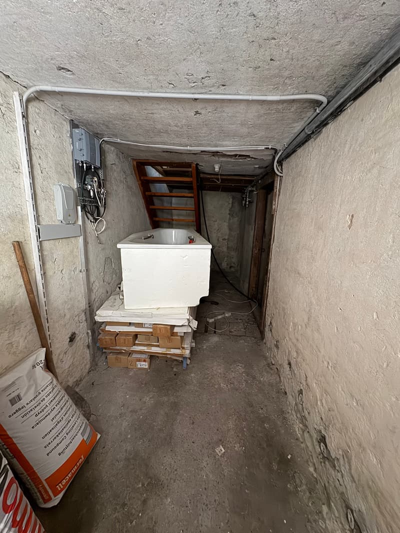 Basement with a concrete floor, wooden staircase, electrical box, bags, wires