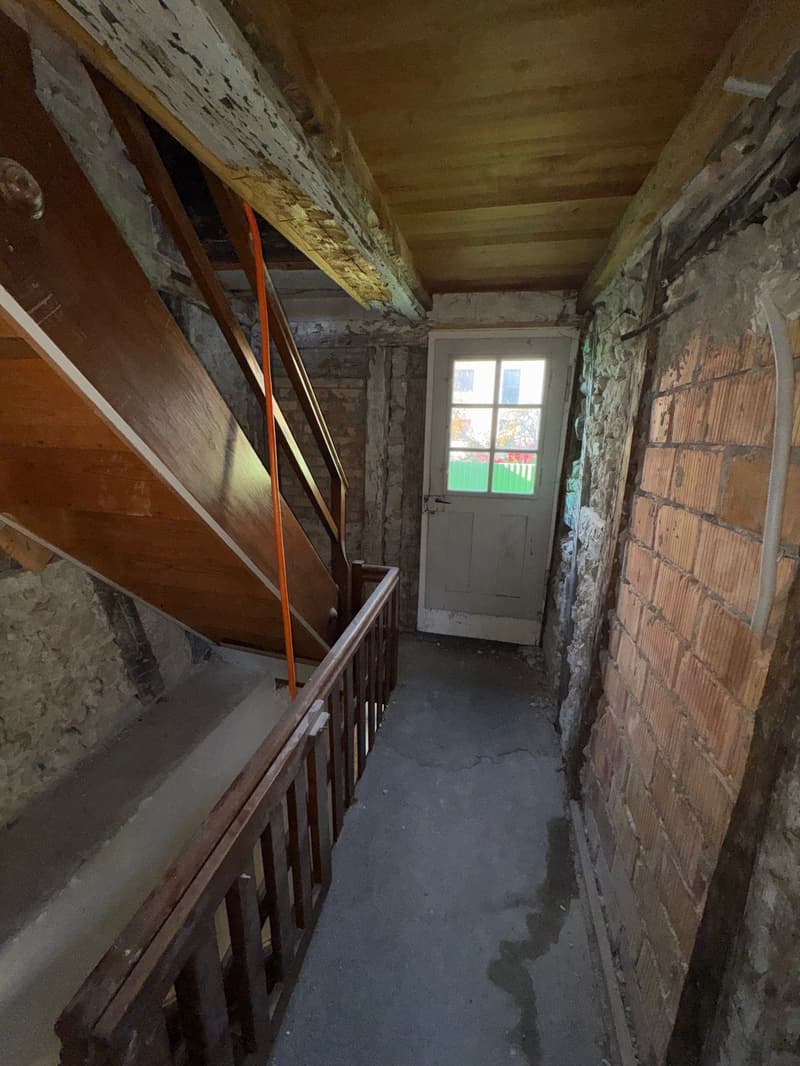 narrow hallway, brick walls, wooden staircase, white door, unfinished floor