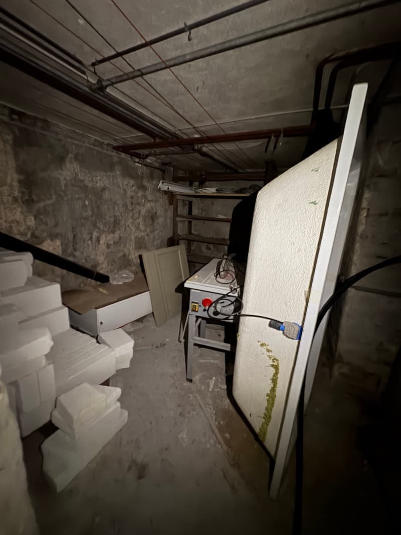 Basement with stone walls, white items, wires, shelves, stairs, table