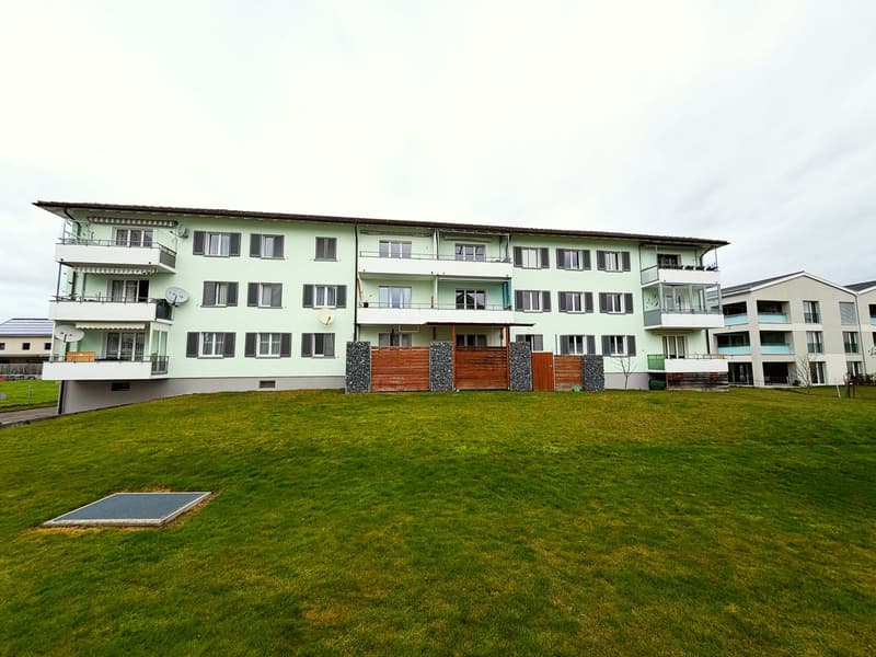 3 story apartment building, green exterior, multiple balconies, large grassy area in front
