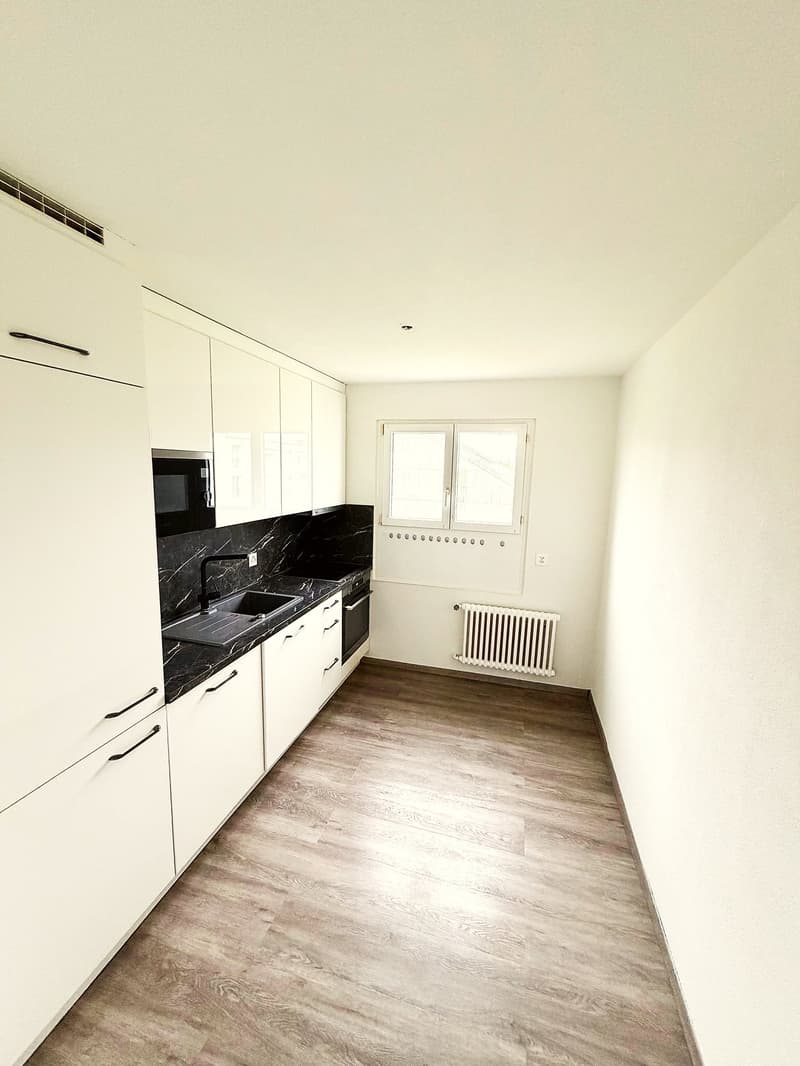 modern kitchen with white cabinets, black marble countertop, wooden floor, white walls, window, white radiator, black microwave, sink, faucet, black stove
