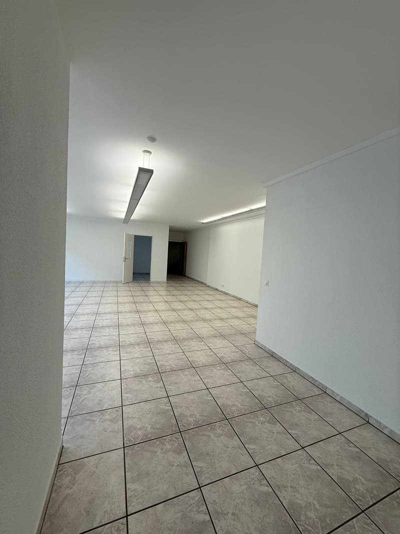 Empty room with white walls, ceiling lights, tiled flooring, and two doors.