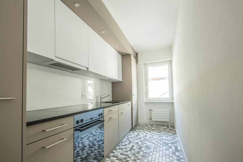 modern kitchen with white cabinets, black countertop, integrated oven and dishwasher, sink with faucet, window