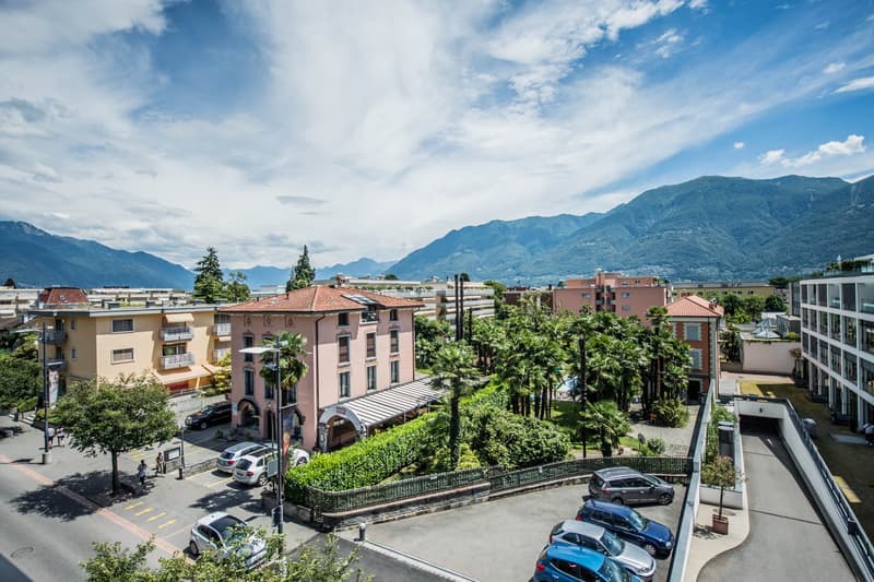 Aerial view of a building with a parking lot, surrounded by trees and mountains in the background.