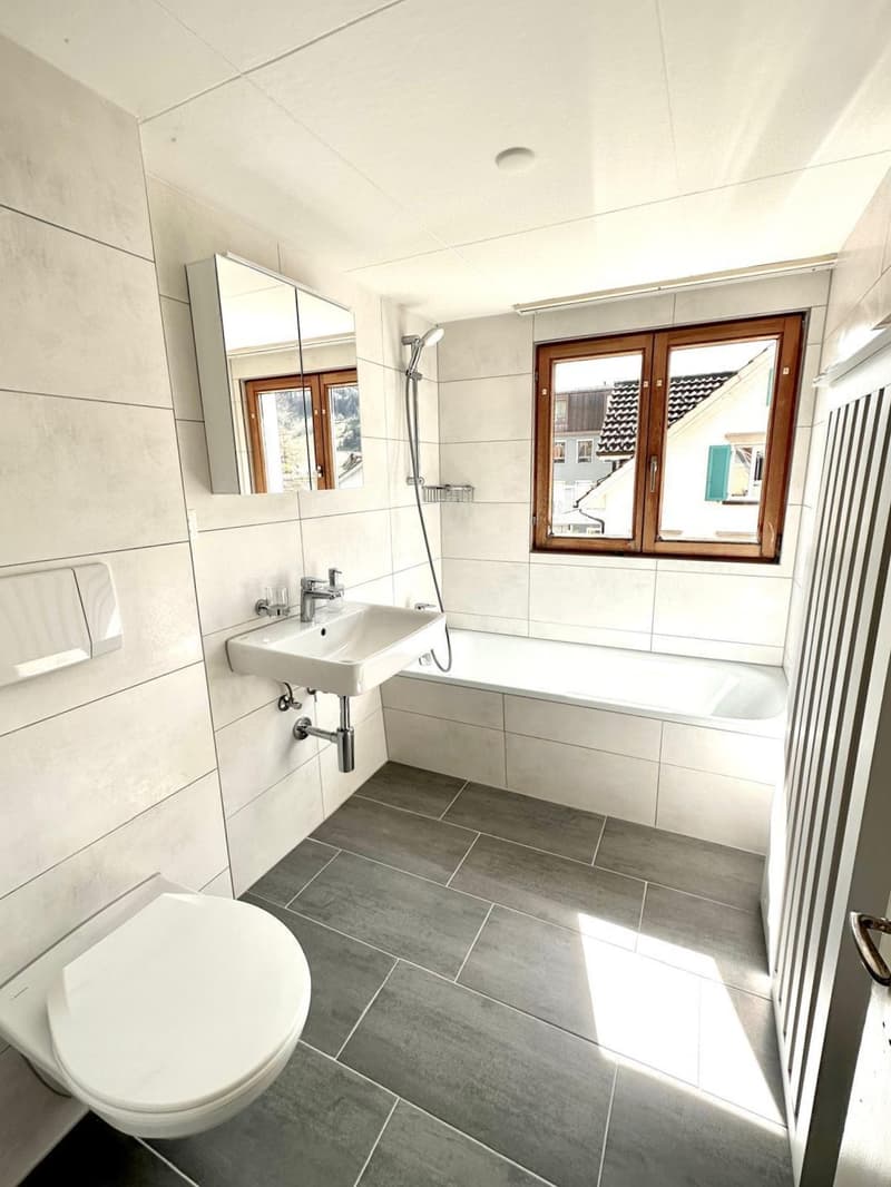 modern bathroom with white tiles, bathtub, sink, mirror, and toilet