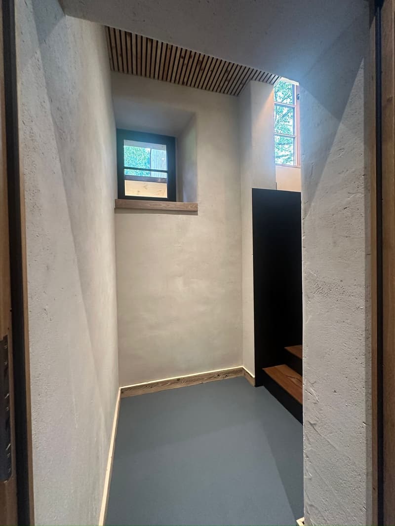 empty room, small window, wooden bench, white walls, grey floor