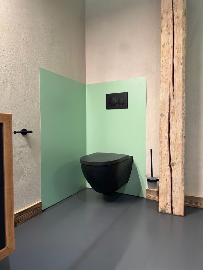 Compact modern bathroom with wall-mounted toilet, white and green walls, floor level slightly higher, wooden pillar