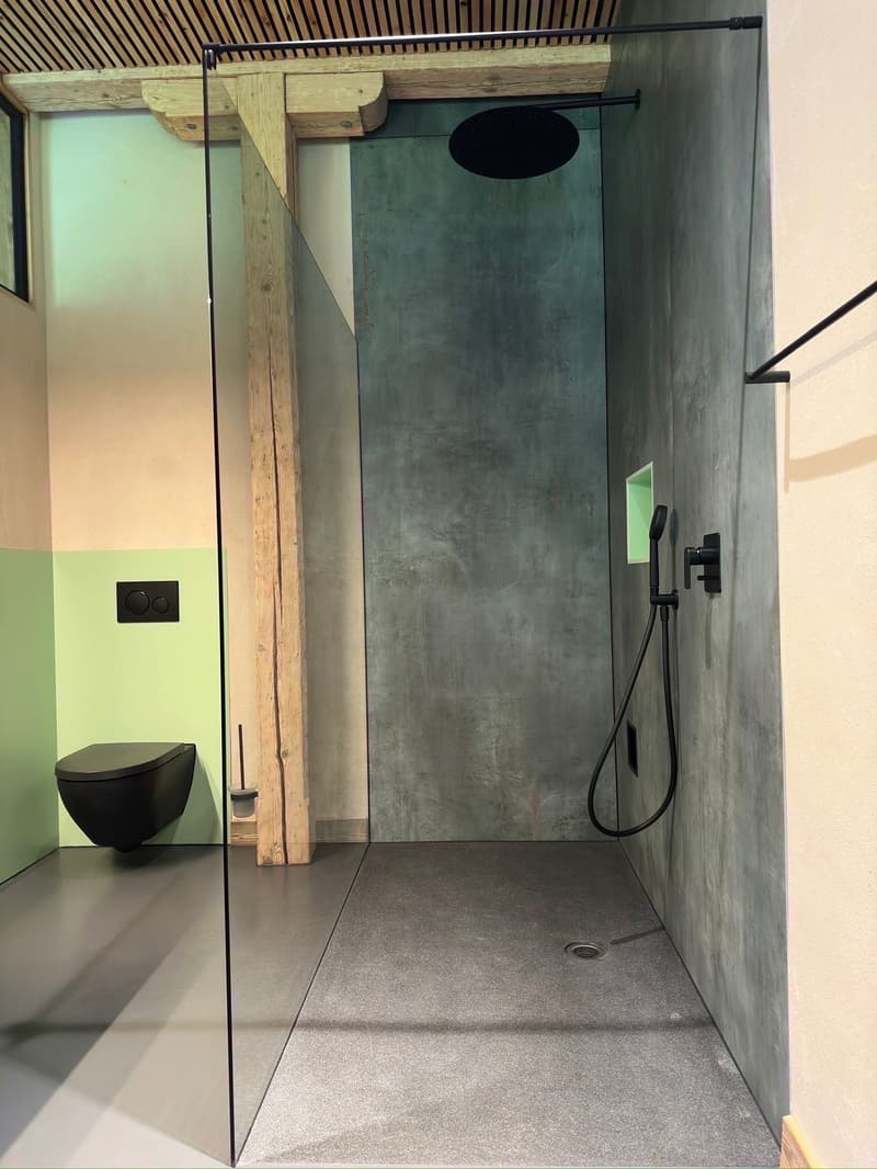 Modern bathroom with walk-in shower, glass door, black toilet, green wall, wooden beam