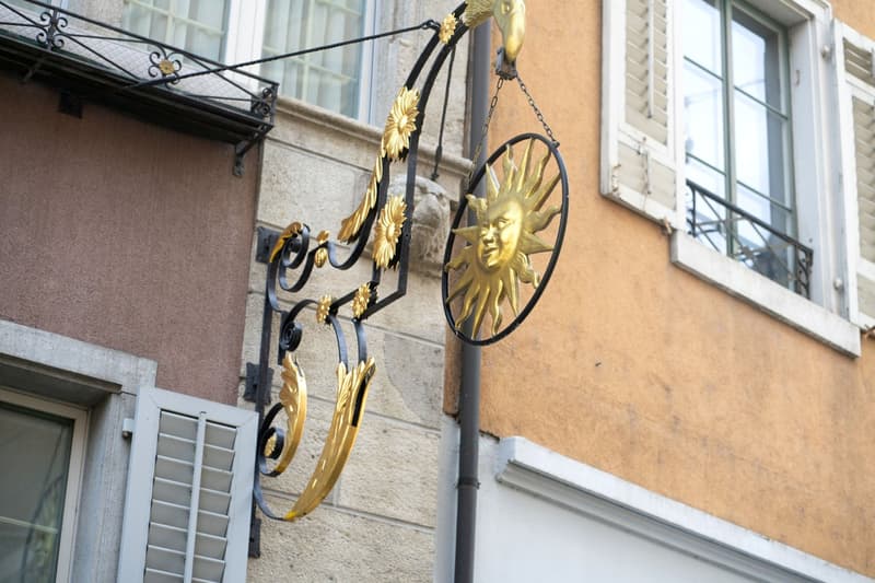 Black and gold decorative sign with a sun emblem hanging from a building.