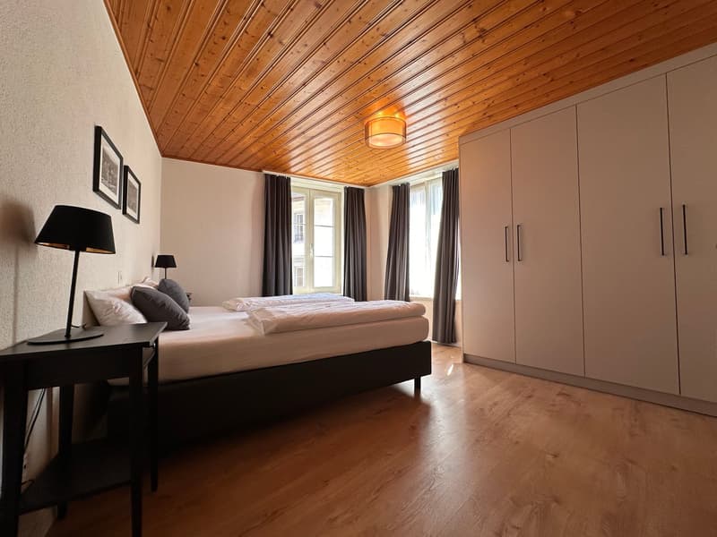 modern room with wooden ceiling, large bed, lamps, cabinets, bedside table
