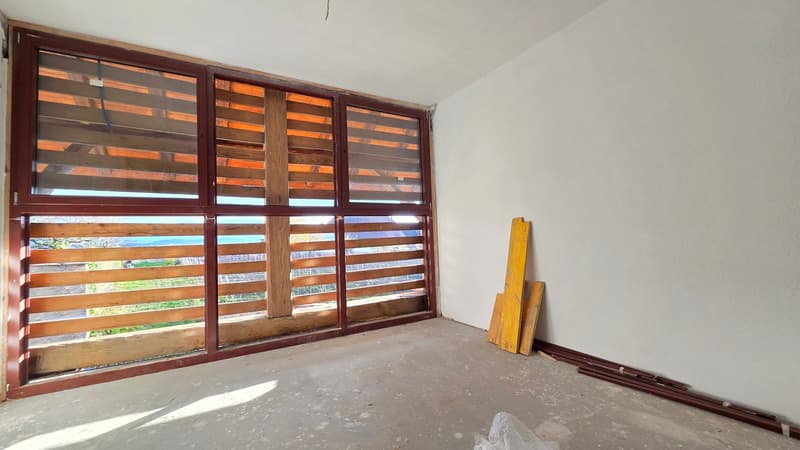 Large windows leading to balcony, concrete floor, wooden slats, white wall