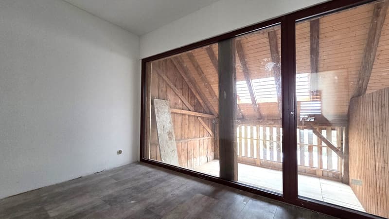An empty room with wooden floors and sliding glass doors opening to balcony with wooden railings