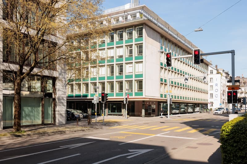 white building with green windows, multiple floors, trees, street lights, traffic signals, cars parked in front