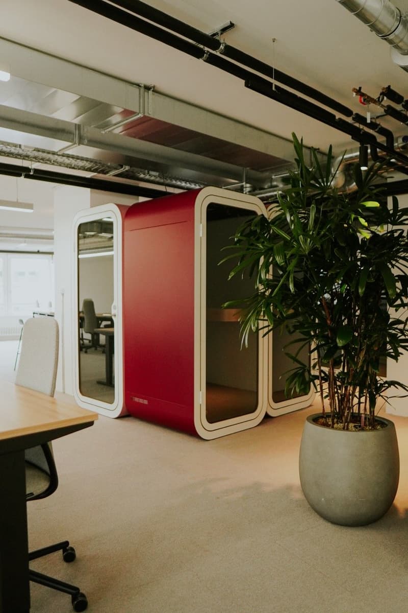 Modern office space with red and white furniture, potted plants, and exposed ceiling pipes and ductwork.