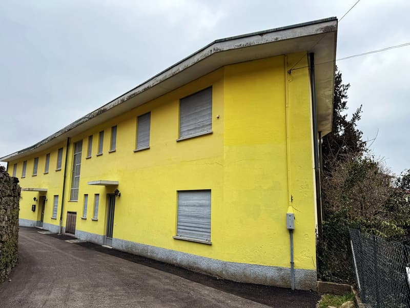 A multi-story yellow building with windows and roller shutters. The building has a flat roof and appears to be in a residential or commercial area.