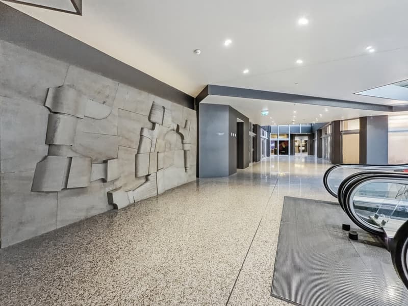 Concrete wall with abstract design, polished concrete floor, escalator, gray carpet, white ceiling with lights