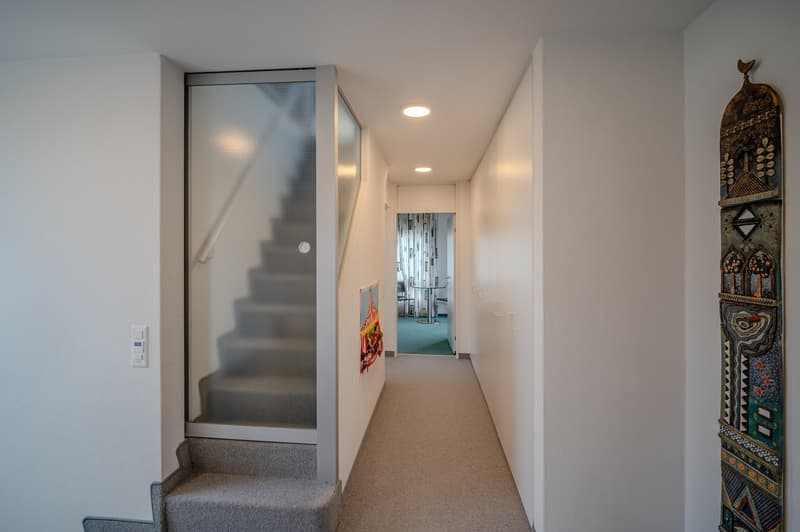 modern hallway with white walls, gray carpet, glass door, and staircase