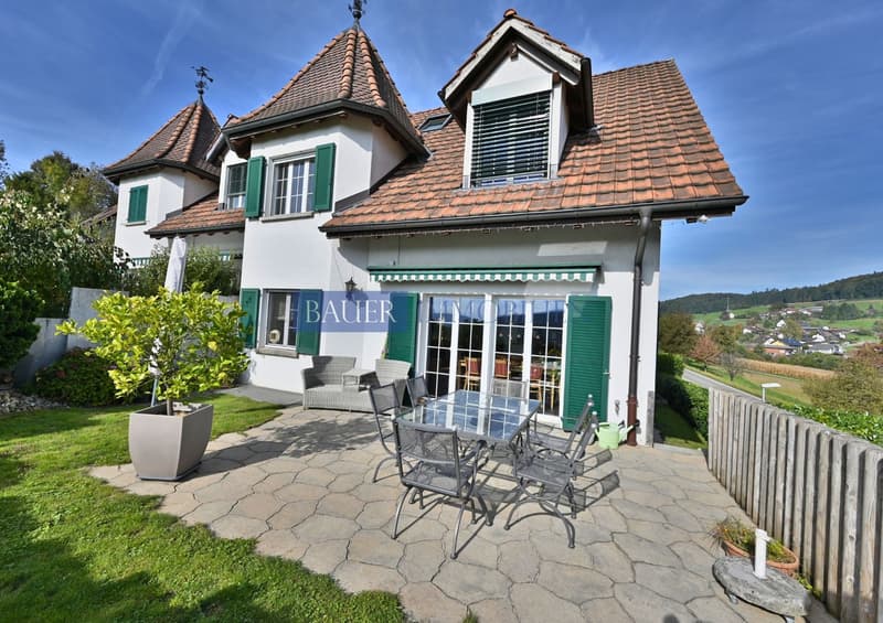 white two story house, brown roof, green shutters, large windows, garden, patio with table and chairs, view of surrounding countryside