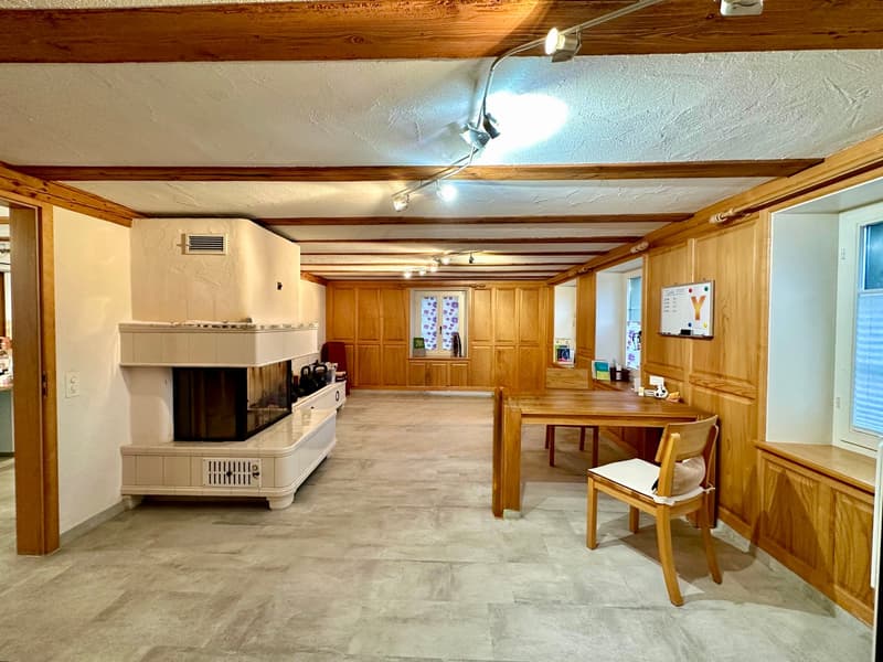 Spacious room with wooden walls, fireplace, wooden desk, chair, ceiling spotlights, ceiling paneling, white tiled floor