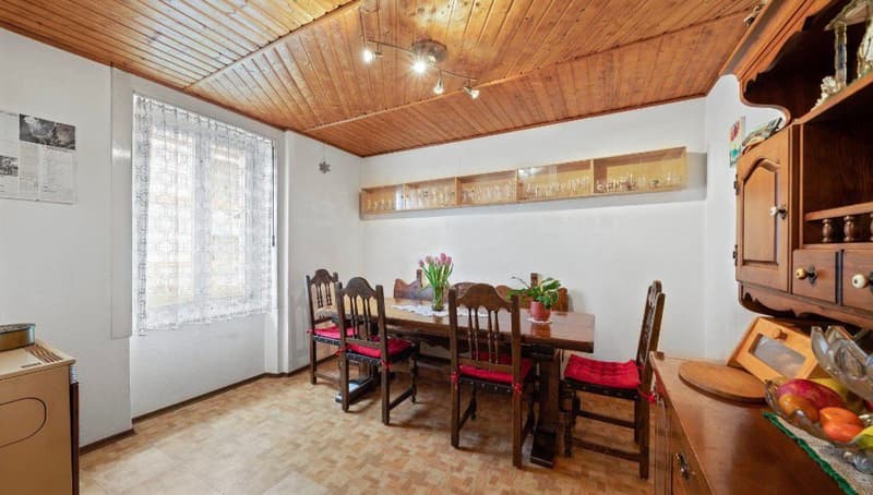 Dining room with wooden table, chairs, wooden cabinet, wooden ceiling, white walls, window with curtains
