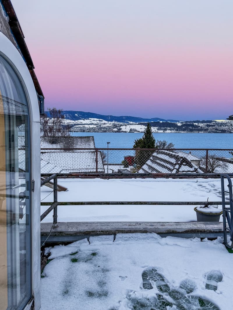 House with balcony, snowy landscape, mountains in the distance, lake, fence