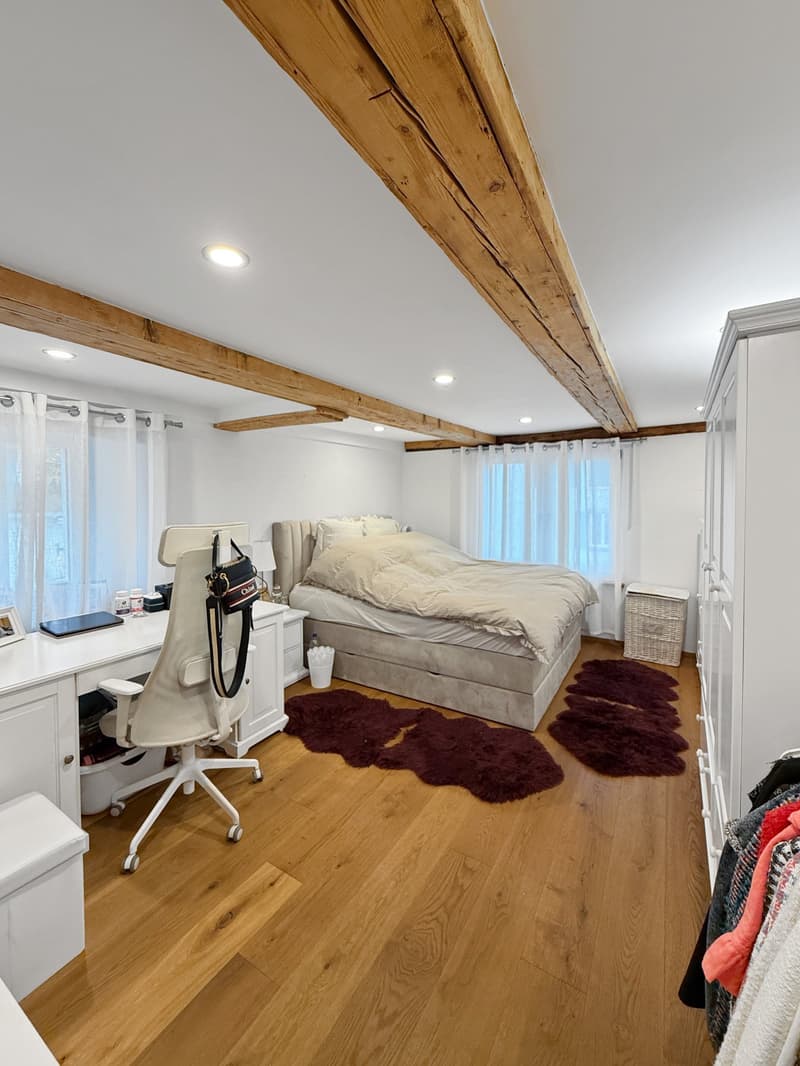 bedroom with wooden beams, wooden floor, white walls, bed, desk, chair, rug, wardrobe