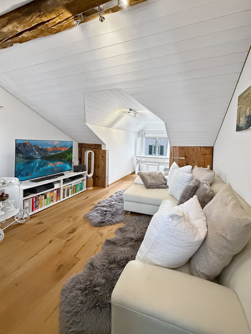 A cozy living room with a white couch, a flat screen TV, a wooden floor, and a wooden ceiling.