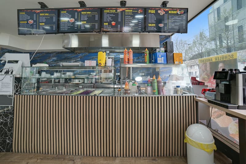 Counter with condiments, menu boards, glass display case, trash bin, coffee machine, and a glass wall.