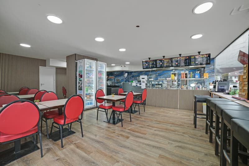 Wooden floor, red chairs, tables, counter, refrigerators, menu boards, stools