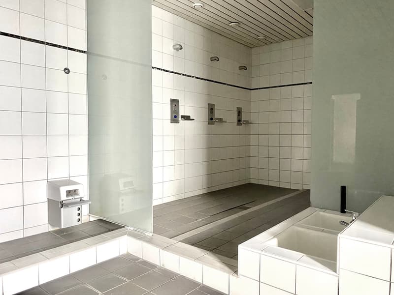 Large bathroom with white tiled walls, raised tiled floor, and built-in shelves. There is a bathtub and a separate shower area.