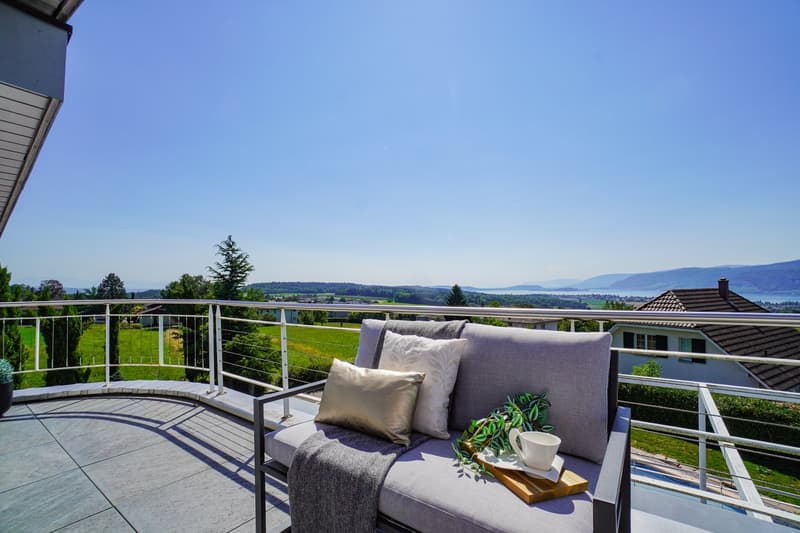 Modern outdoor living area, furniture and greenery, balcony with fence and railings, expansive view of the countryside