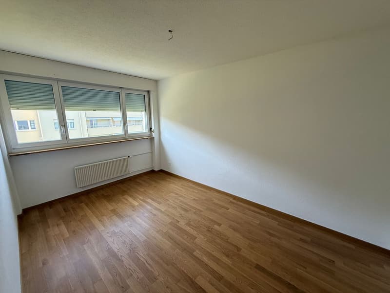 Empty room with wooden floor, white walls, large window, and a white radiator.