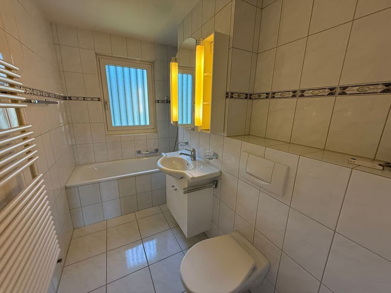 Bathroom with white tiles, bathtub, sink, toilet, and mirror.