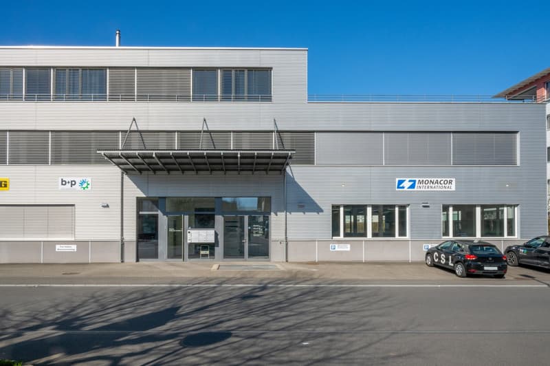 2 story commercial building with glass entrance, white exterior, 3 cars parked in front, Monacor International sign
