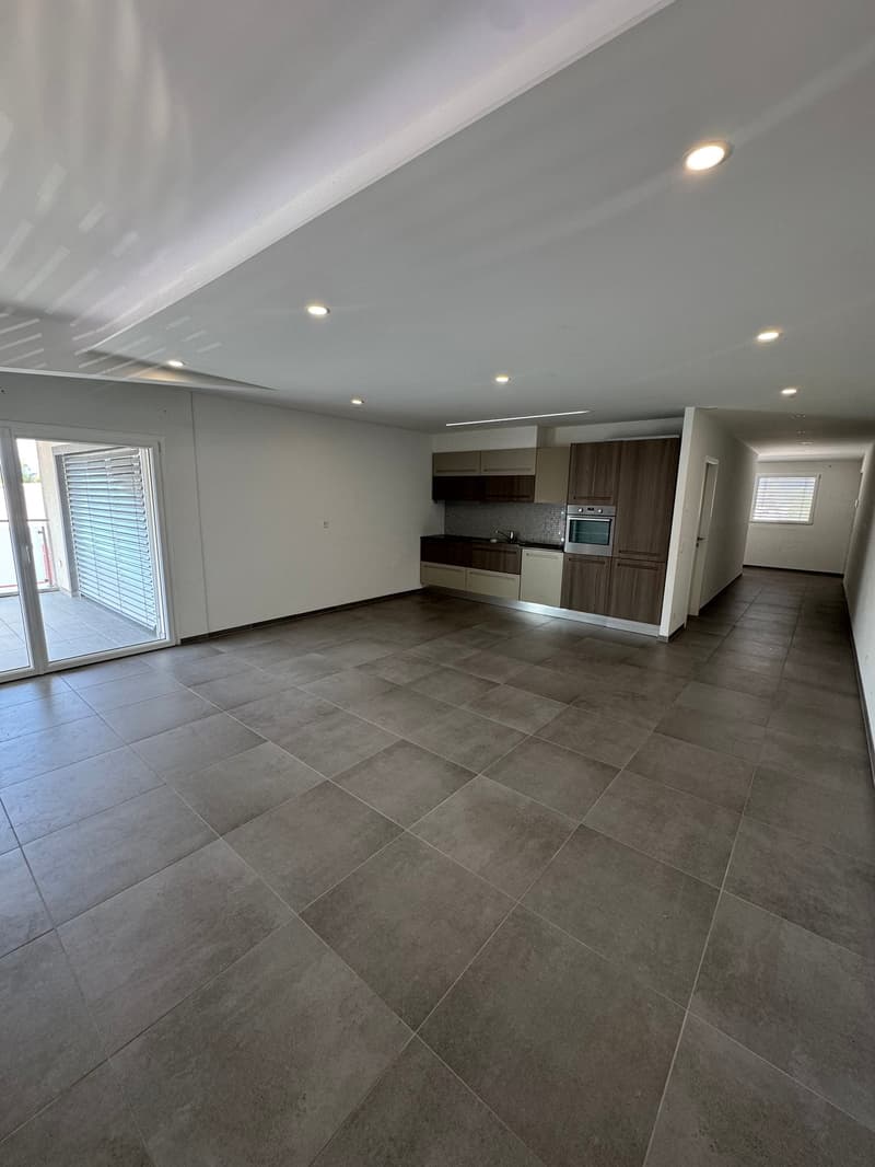 Open-concept living space with a modern kitchen, hardwood floors, and recessed lighting. The room has a sliding glass door leading to an outdoor area.