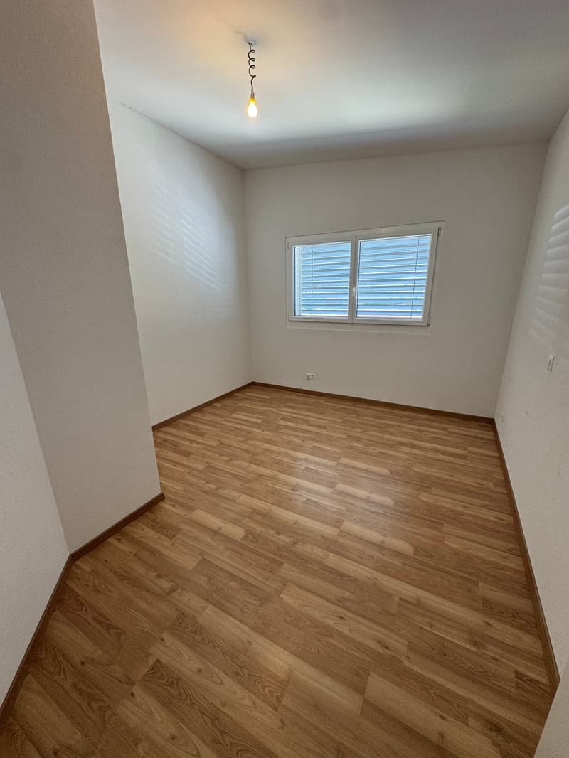 Empty bedroom with white walls, hardwood flooring, and a single window with blinds.