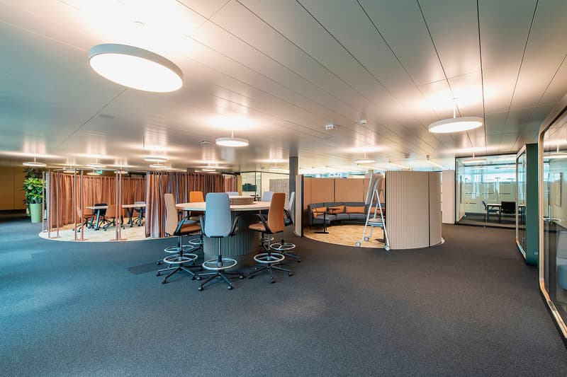 modern office space with round table, chairs, round couch, glass walls, carpet, lamps