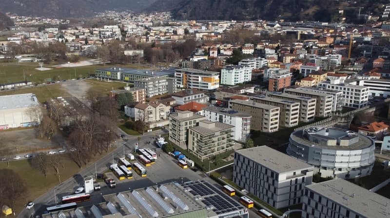 Aerial view of a city with many buildings, some with solar panels, a bus station, and a road with cars and buses.
