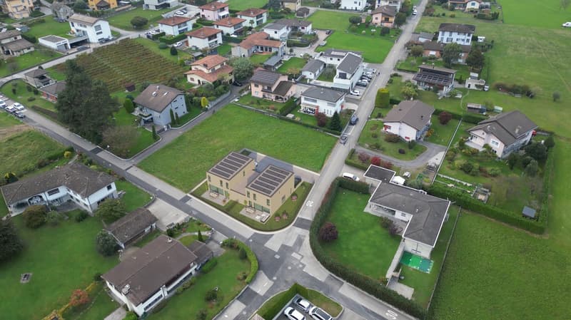 Multi-family house neighborhood, several houses with solar panels, driveways, well-maintained green lawns, cars parked