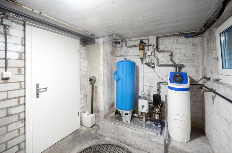 A basement room with a white door, brick walls, and various water treatment equipment.