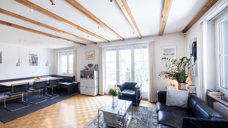 living room with wooden floor, wooden beams, white walls, large windows, black leather couch, glass table, black chairs, black rug, white curtains, potted plant, picture frames, radiator