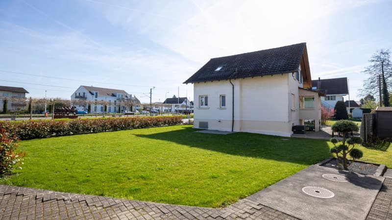 Detached house, white exterior, black roof, large lawn, shrubs, paved walkway, trees, street view