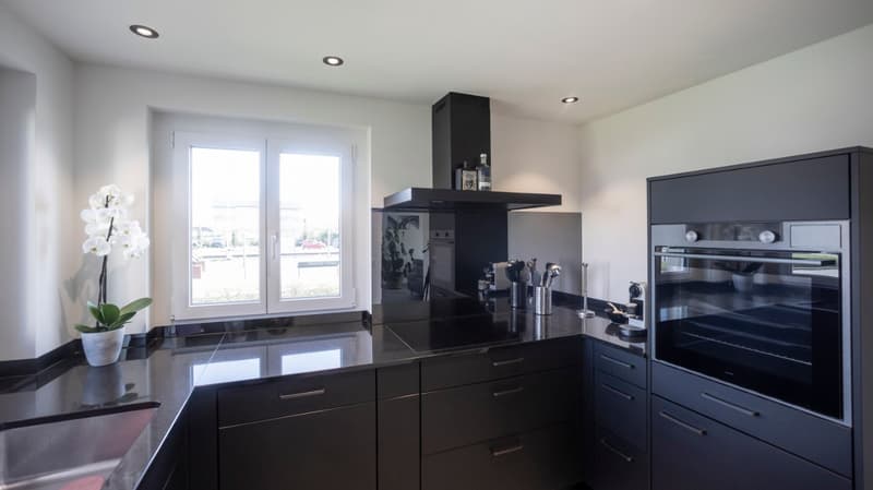 modern kitchen with black countertops, black cabinets, black stove, black oven, white walls, large window