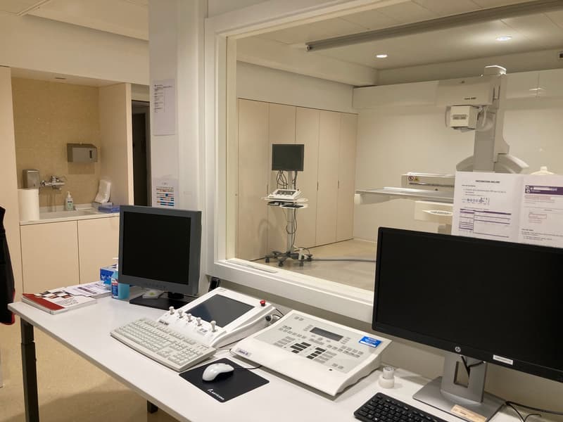 Office room with desk, computer monitors, keyboard, mouse, medical equipment, books, and papers